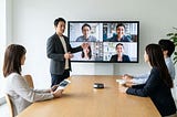 Manager leading a virtual team meeting while remote and in-office employees share stories on a video call