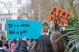 Two people hold up signs at a protest ‘it’s a dress not a yes’ and ‘stop blaming the victim’. Photo by <a href=”https://unsplash.com/@theeastlondonphotographer?utm_source=unsplash&utm_medium=referral&utm_content=creditCopyText">Ehimetalor Akhere Unuabona</a> on <a href=”https://unsplash.com/s/photos/feminism?utm_source=unsplash&utm_medium=referral&utm_content=creditCopyText">Unsplash</a>