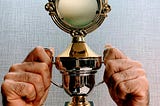 Two hands holding a tiny trophy that barely fits around his fingers