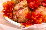 Scones with pink sanding sugar sitting on a white plate with orangey-red flowers dotted between the scones. Sitting on a soft peach background. Inspired by the Featherington sisters