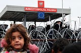 A girl stands next to the Belarusian fence as several Polish police officers stand guard at the Bruzgi-Kuznica Bialostocka border crossing, near the Belarusian-Polish border, on November 15, 2021, in Bruzgi, Belarus. Viktor Tolochko/Sputnik (Europa Press via AP)