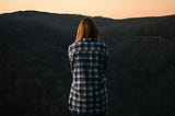 Woman wearing blue and white plaid dress shirt in front of green mountain.