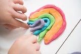 Two hands making a rainbow out of playdough