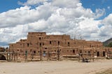 Taos Pueblo occupies the whole image space with fluffly white clouds and blue sky in the background.