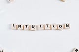“Word ‘intuition’ spelled out with Scrabble tiles on a white background.”