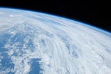 A photograph of Earth taken from the International Space Station. It shows a vast expanse of blue sea and cloud cover.