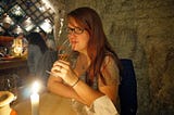 Author with long red hair and glasses drinking wine in a basement wine cave in Budapest during her travels