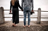 A man and woman hold hands and gaze out at the ocean