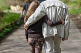 A grandfather takes a walk with his granddaughter with their hands wrapped around each other.