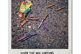 Crayons scattered on the pavement next to their crushed box