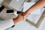 Two women shaking hands over a desk.