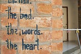 Painted Inscription on a wall of red bricks — It’s All Messy. The Bed. The Words. The Heart. Life.