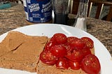 An open peanut butter tomato sandwich featuring the ingredients in the background.