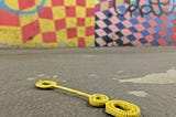 A discarded yellow bubble wand lies on the ground of a NYC subway tunnel. Brilliant painted checkerboard walls with graffiti in the background.