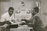 Jackie Robinson sitting at a table in a scene from a movie where he played himself in “The Jackie Robinson Story” (1950).