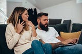 Happy young couple using a laptop and a smartphone while researching water cremation.