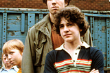 With his arms folded, actor Chris Makepeace stands in front of an angry looking Adam Baldwin, while Paul Quandt peeks out from behind Adam Baldwin, in a scene from the 1980 movie My Bodyguard. The movie about a boy who acquires the services of the school’s most feared kid as his  bodyguard.