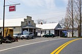A view down a rural,two-lane road showing two small, local businesses on the left, including a garage with a Toro sign.