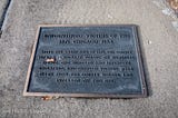 A metal plaque lays on a concrete walkway.