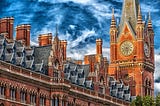 Sunlit clocktower made of russet brick against a blue sky with swirling white clouds in the United Kingdom.