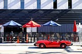red convertible in front of outdoor seating with red and blue umbrellas