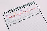 Top spiral bound graph paper with “New Year’s Resolutions” in all capital letters and red ink is written across the top. Small doodles of stars, hearts, and smiley faces in different colored ink surround the title. Below this, many pages have been ripped out, revealing a page with the following written in black ink: “1. Quit Making New Year’s Resolutions”