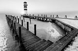 A lighthouse at the end of the pier during a winter sunset shot in black and white.