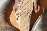 African male feet, a converse shoe and gumboots with soil in the background.