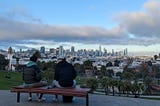 2 people sitting on a bench looking over Dolores park and downtown San Francisco