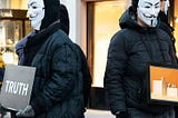 two persons with Guy Fawkes masks holding signs stating truth and ethics