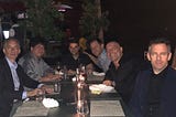 Jordan Peterson, Eric Weinstein, Ben Shapiro, Dave Rubin, Joe Rogan, and Sam Harris sitting at a table together in a dining or drinking establishment.