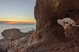 Stone arch by the ocean and sun is setting.