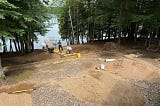 Hillside to a lake with a dock having a walkway built, surrounded by stone.