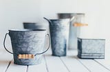 tarnished silver buckets of varying size sitting on a white wooden floor.