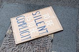 Image of a protest sign on the ground saying “to be silent is to be complicit”
