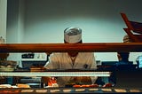 A cook assembling a sandwich with their face hidden behind a counter