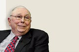 Charlie Munger, dressed in a black suit, striped shirt, and a red / blue striped tie