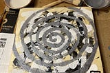 An encaustic painting on a wooden board, consisting of black and white scoring, overlaid with a silver spiral.