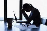 Woman sat at her deak in front of a laptop with her hand in her hands