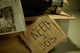 A cardboard sign saying “NEED A JOB”