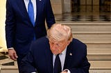 A photo of President Trump signing the MOU at Versailles Palace while Secretary of State Rubio looks on.
