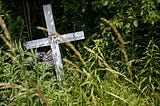 weathered wooden cross surrounded by weeds