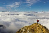 A man standing atop a mountain overlooking a canopy of clouds