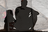 A father and daughter sit together on a hilltop looking out toward the horizon and are silhouetted from this perspective. Layered beneath the image is another image of books and dried roses across the books.