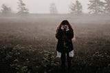 A woman stands in a field with her head in her hands.