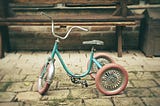 Foto de um velho triciclo azul e com rodas vermelhas. A imagem traz a ideia de uma memória da infância.