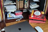 A desk with an Apple laptop, a dictionary, and grammar books.