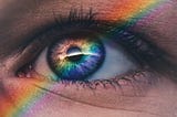A close up image of an eye with a spectral ray refracted across it, lighting up the iris in all the colours of the rainbow