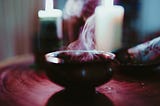 Smoke coming out of a cauldron in front of candles.