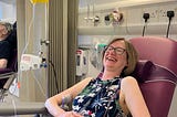 A woman in a hospital chair with an IV in her arm, laughing